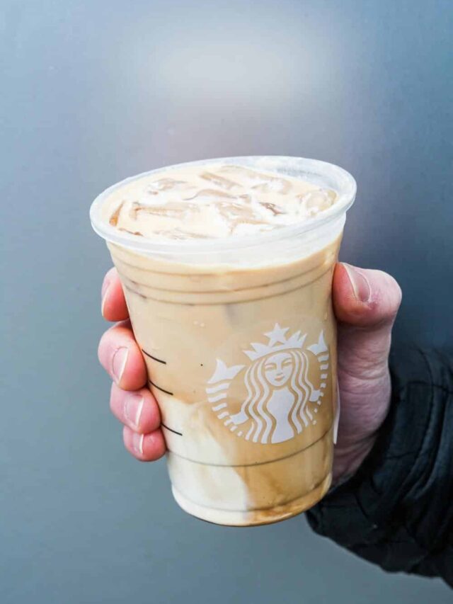 A hand holding a clear cup of Starbucks iced latte.