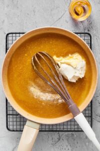Cream cheese, broth, and a whisk in a pot on a wire rack.