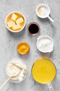 A picture of broth, a bowl of cream cheese, a bowl of cornstarch, a bowl of mustard, bowl of soy sauce, a bowl of butter, and a bowl of seasonings all on a Gray counter.