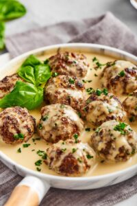 A few gluten-free meatballs that have a white gravy on top of them sitting in the white gravy that is on a white plate..