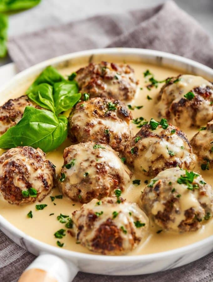 A few gluten-free meatballs that have a white gravy on top of them sitting in the white gravy that is on a white plate..