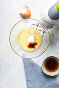 Electric mixers in a bowl that has beaten egg yolk, Greek yogurt, and vanilla extract.
