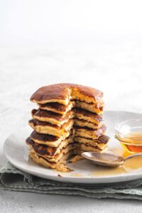 A stack of pancakes that have a piece cut out from the front of them on top of a white plate that has some syrup on it.