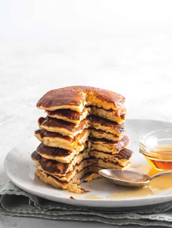 A stack of pancakes that have a piece cut out from the front of them on top of a white plate that has some syrup on it.