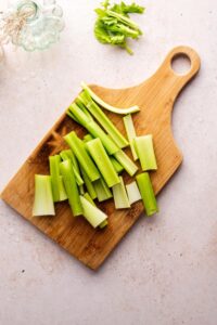 A bunch of pieces of cut up salary on a wooden cutting board on a white counter.