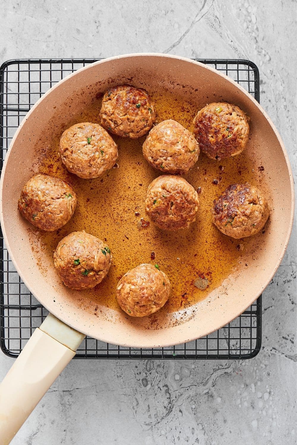 10 meatballs in a skillet on top of wire rack on a gray counter.