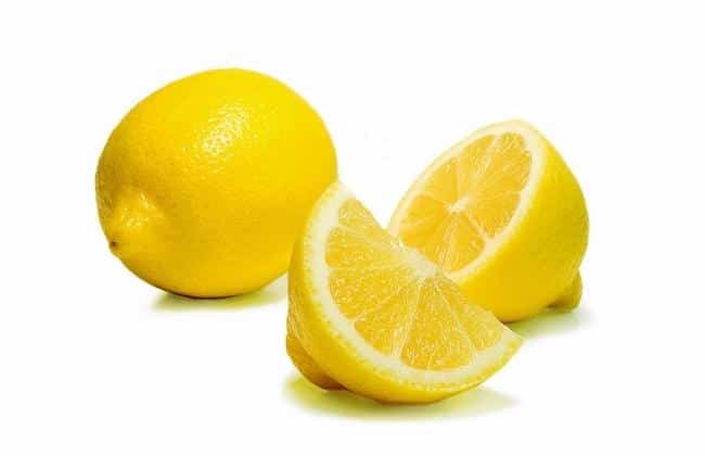 A slice of a lemon in front of another half of a lemon and a whole lemon.