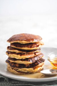 A stack of seven pancakes on a white plate.