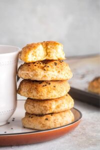 Part of a white plate with for bagels stacked on it with the top bagel having a bite out of it.