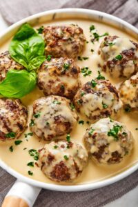 A bunch of gluten-free meatballs covered and gravy on a plate that has a white gravy on it.