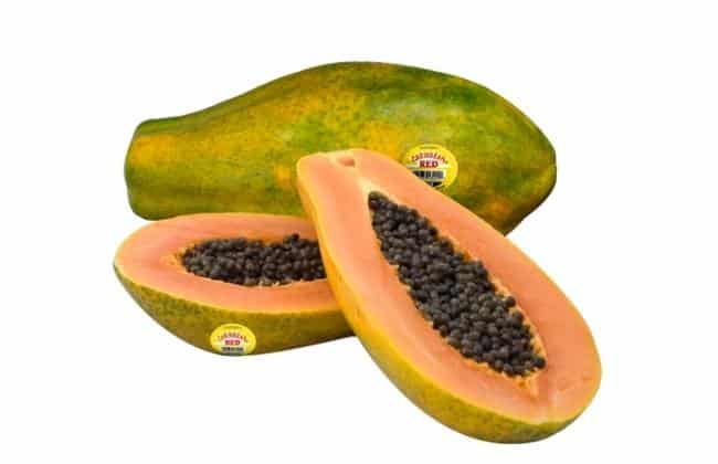 Two halves of a papaya in front of a whole papaya.