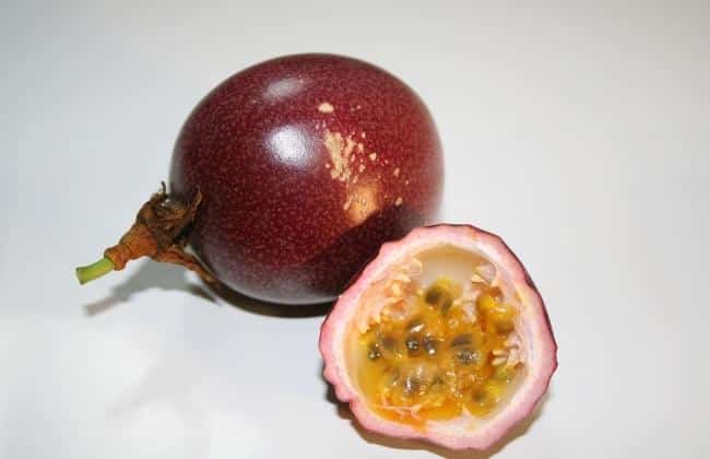 A cut passion fruit in front of a whole passion fruit.