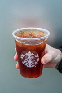 A hand holding a clear cup of Starbucks black ice tea.