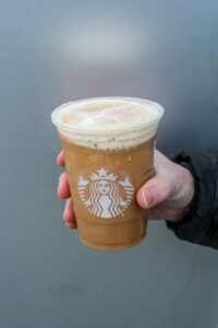 And holding a clear cup of Starbucks iced espresso Frappuccino.