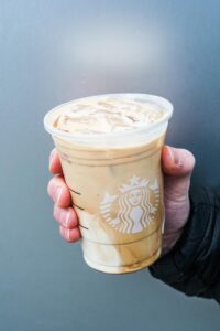 A hand holding a clear cup of Starbucks iced latte.