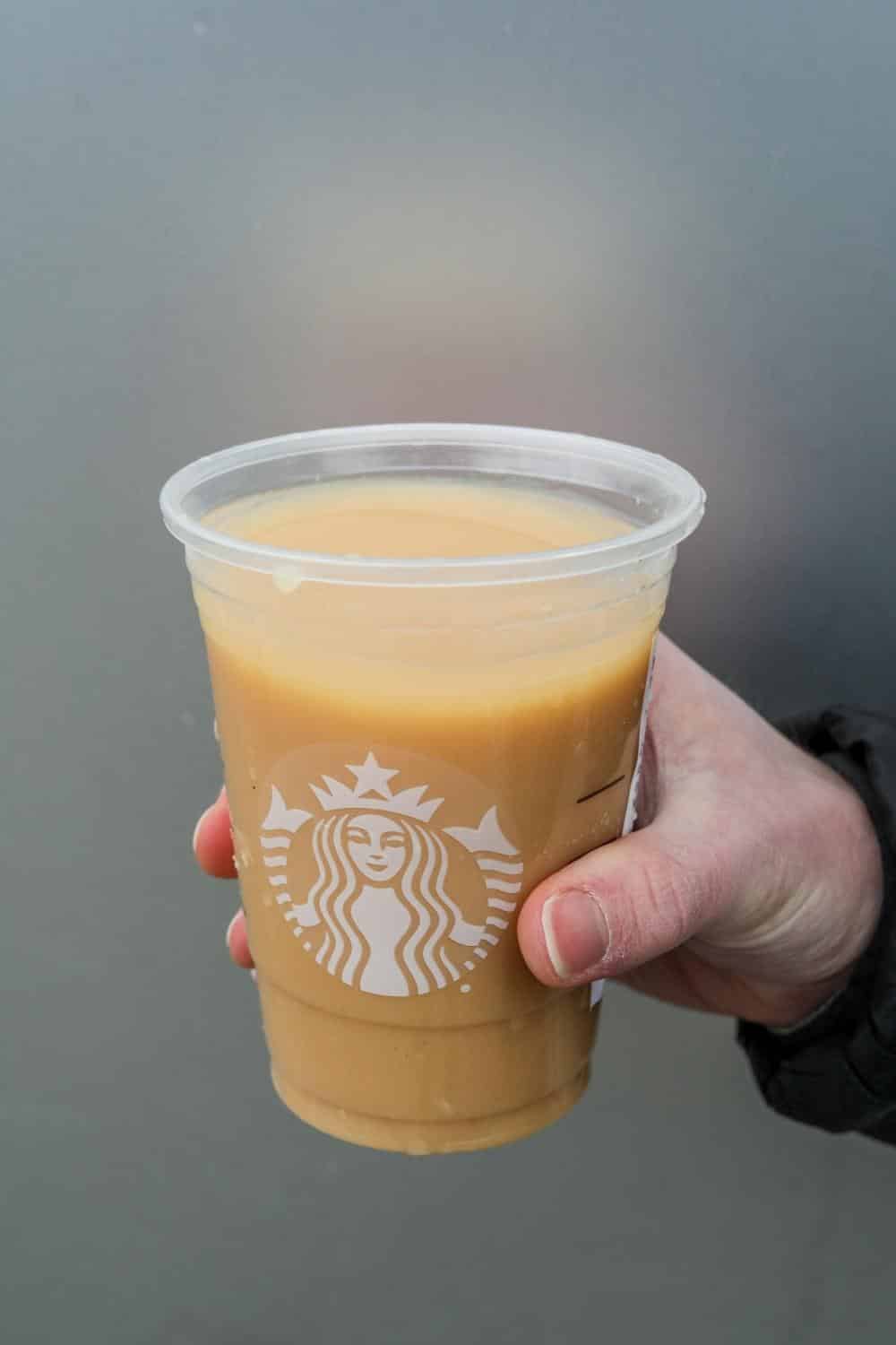 Hand holding a clear cup of Starbucks iced London fog tea latte.