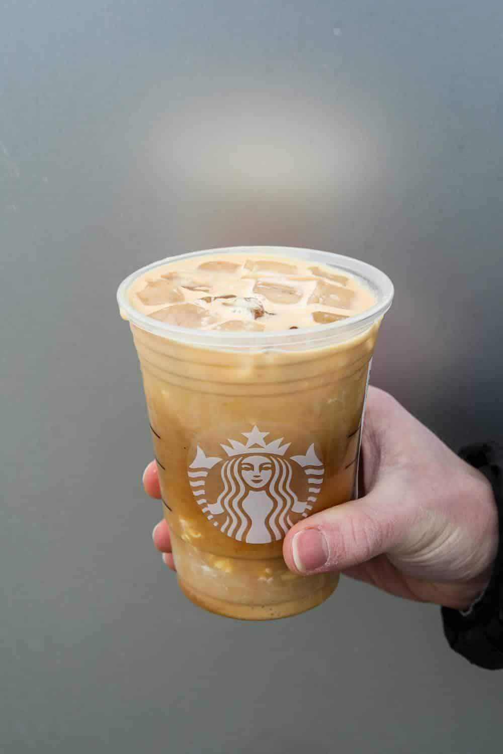 Hand holding a clear cup of Starbucks iced vanilla cream cold brew.