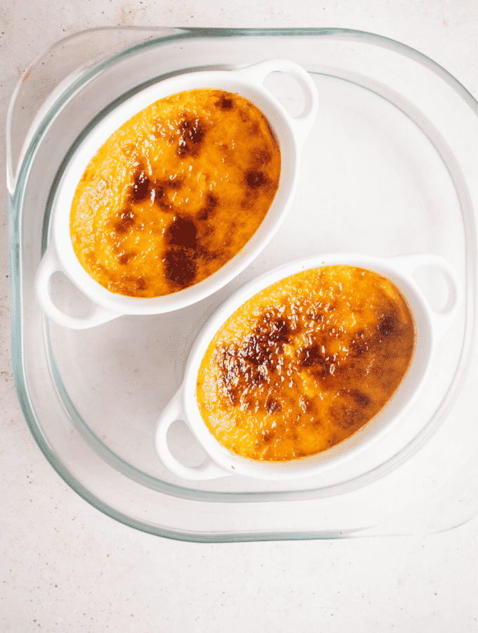 Caramelized crème brûlée in to ramekins in a glass baking dish.