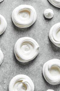 Dollops of meringue on a sheet of parchment paper.