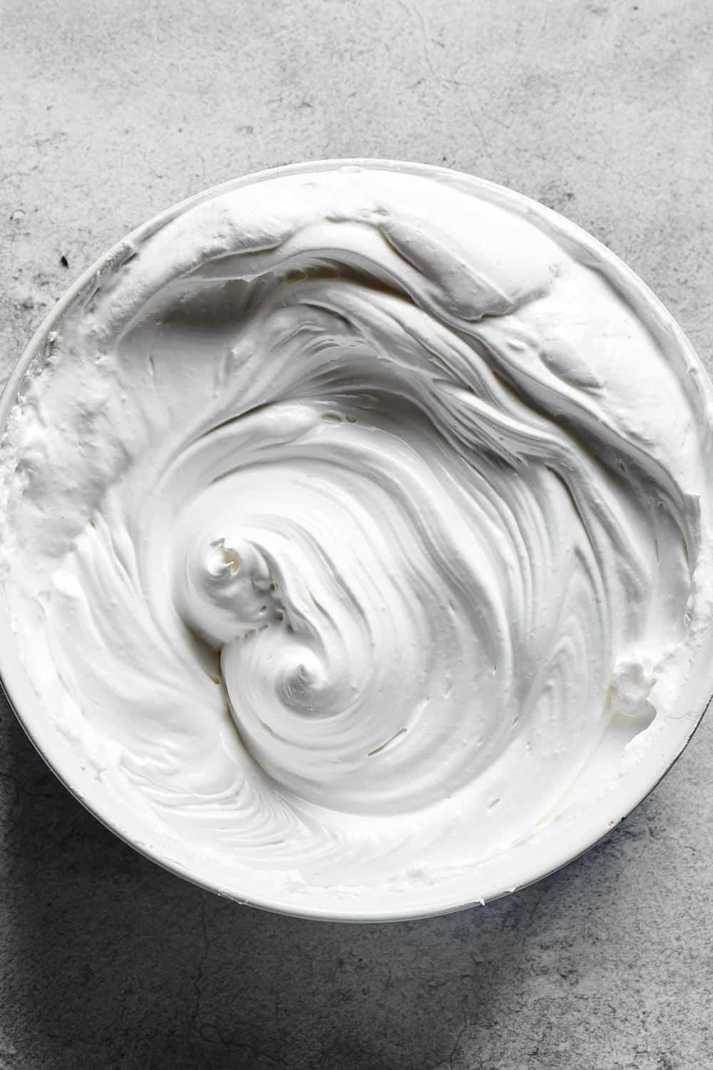 Whipped meringue mixture in a bowl and a gray counter.