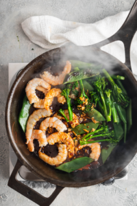 Shrimp, broccoli, and snow peas cooking in a black skillet.