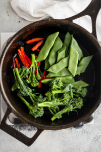 Broccoli, snow peas, and sliced red pepper in a black skillet.