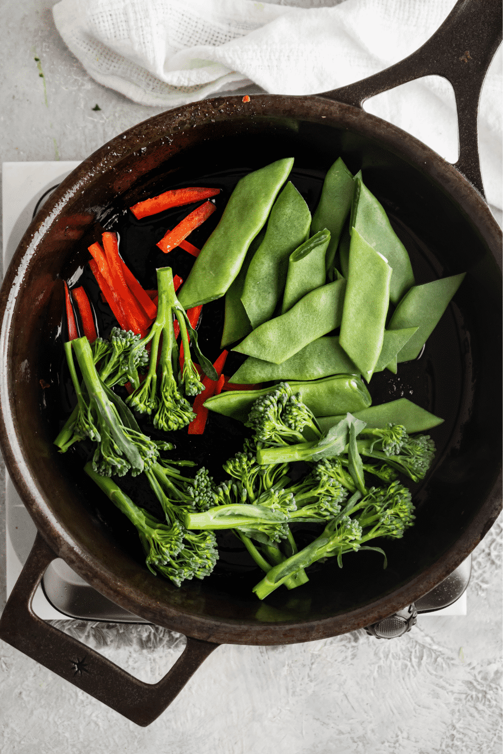 Broccoli, snow peas, and sliced red pepper in a black skillet.