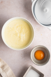 A bowl of melted ice cream and a bowl of an egg yolk on a white counter.