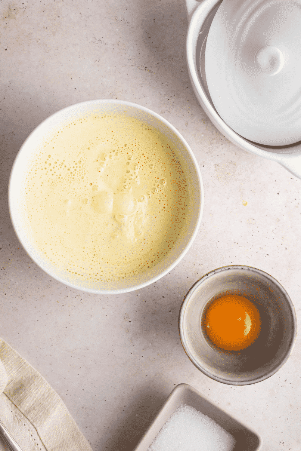 A bowl of melted ice cream and a bowl of an egg yolk on a white counter.