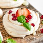 Meringue cookie with a strawberry in the middle and some dried cranberries on it on a wooden cutting board.