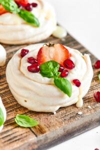 Meringue cookie with a strawberry in the middle and some dried cranberries on it on a wooden cutting board.