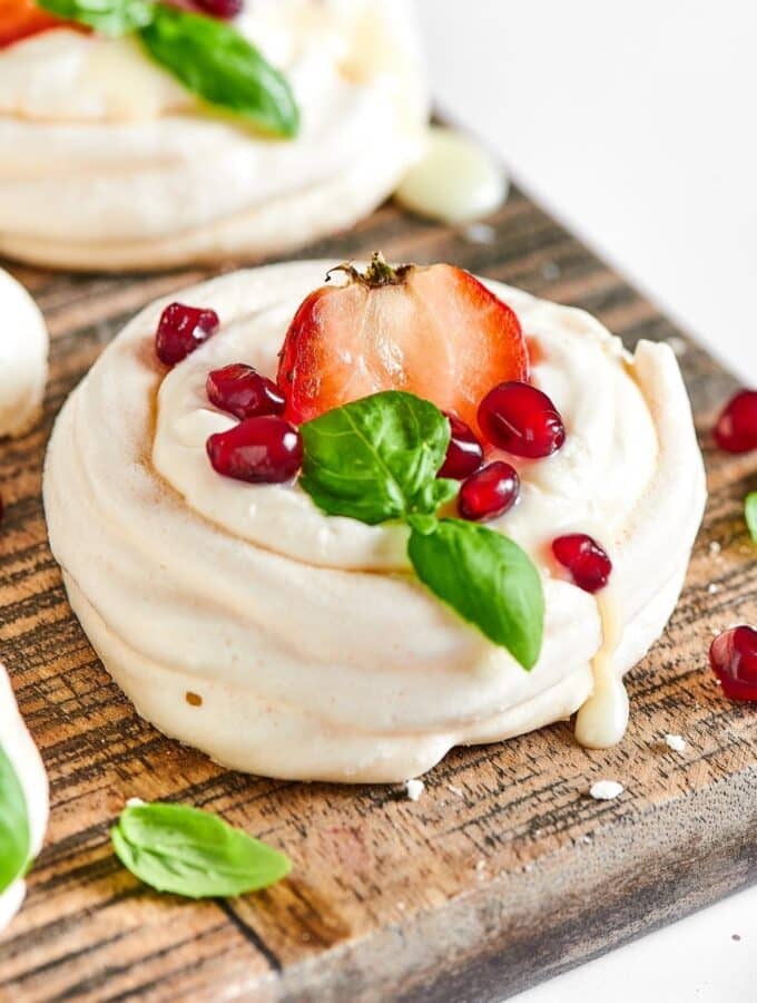 Meringue cookie with a strawberry in the middle and some dried cranberries on it on a wooden cutting board.