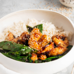 Sesame seeds on top of shrimp, snow peas, broccoli, and white rice in a white bowl.