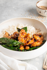 Sesame seeds on top of shrimp, snow peas, broccoli, and white rice in a white bowl.