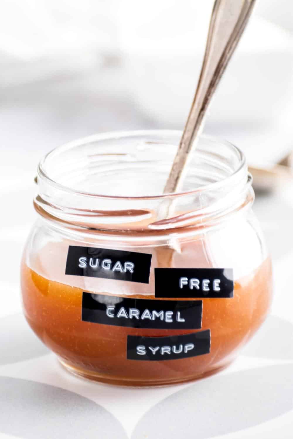A spoon and a glass jar that is halfway filled with caramel sauce.