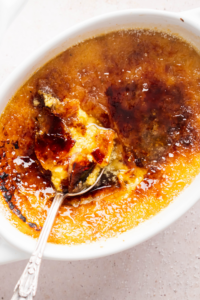 Some crème brûlée on top of a spoon that is on top of crème brûlée in a white ramekin.