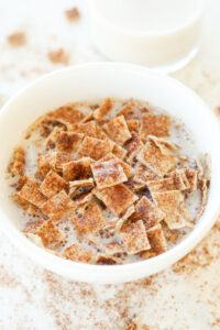 A white bowl filled with cereal and milk. The bowl is set on a white table.