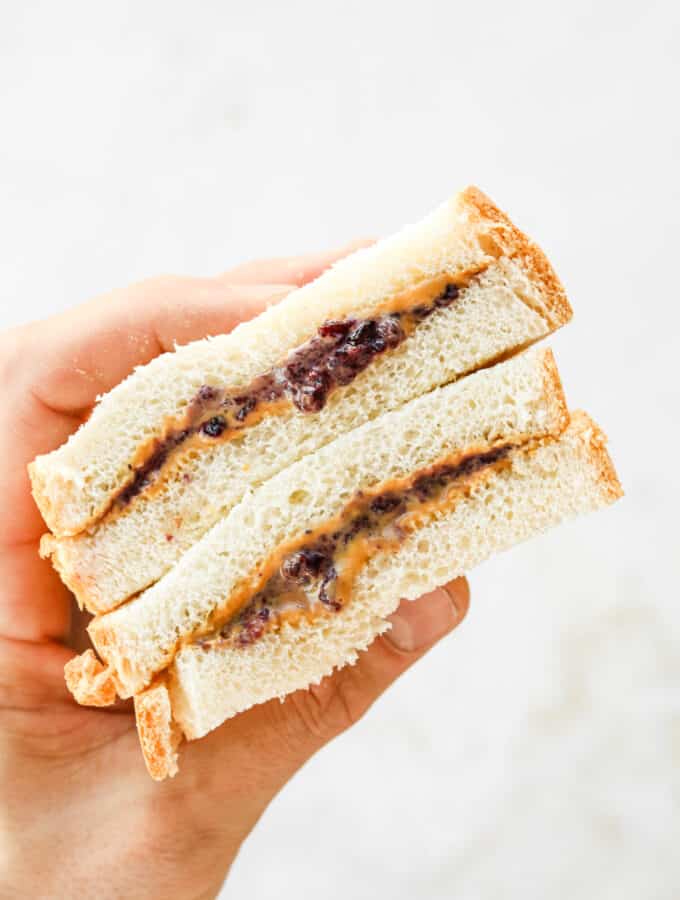 A hand holding a peanut butter and jelly sandwich that's been cut in half.