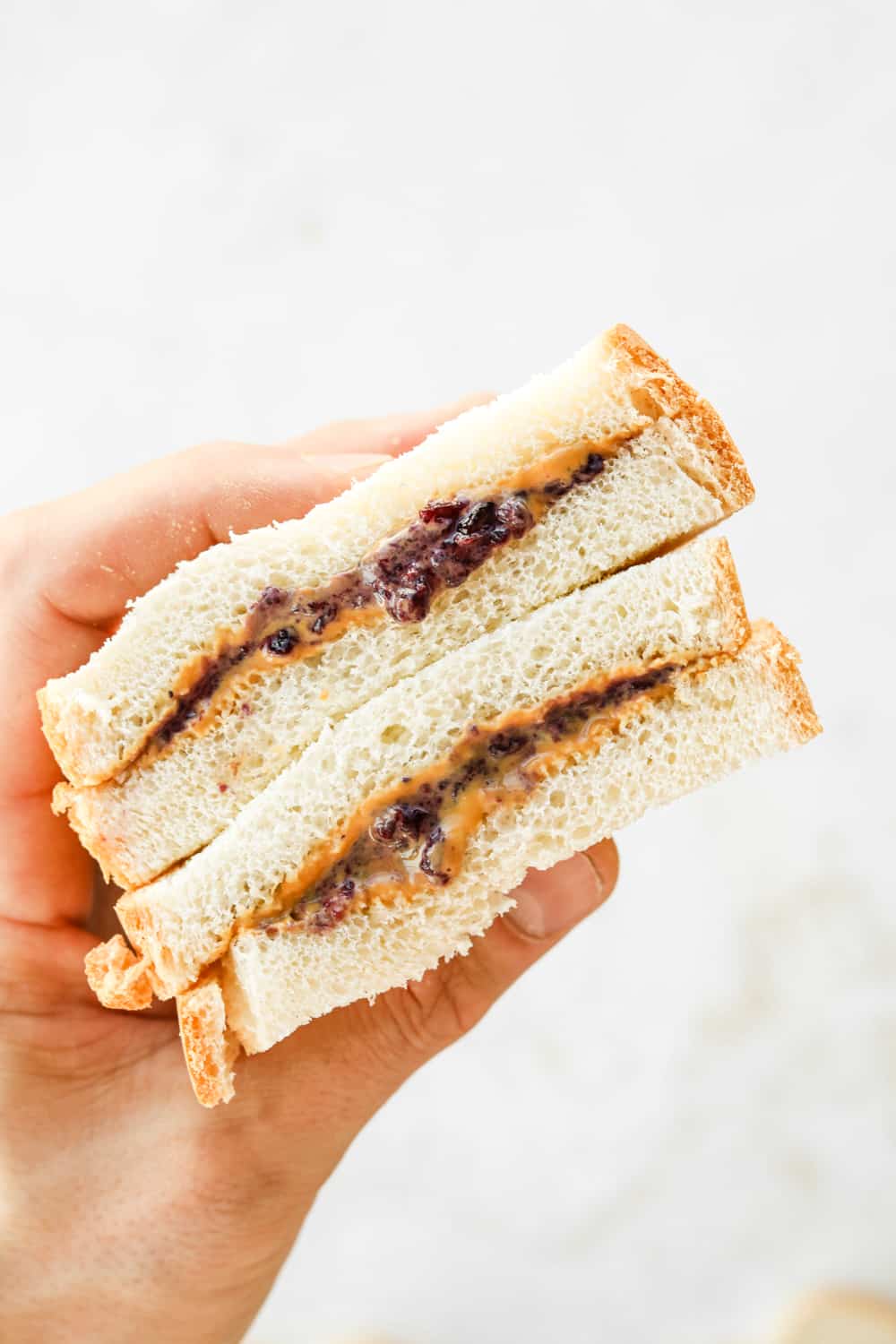A hand holding a peanut butter and jelly sandwich that's been cut in half.