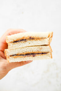 A hand holding a peanut butter and jelly sandwich that's been cut in half.