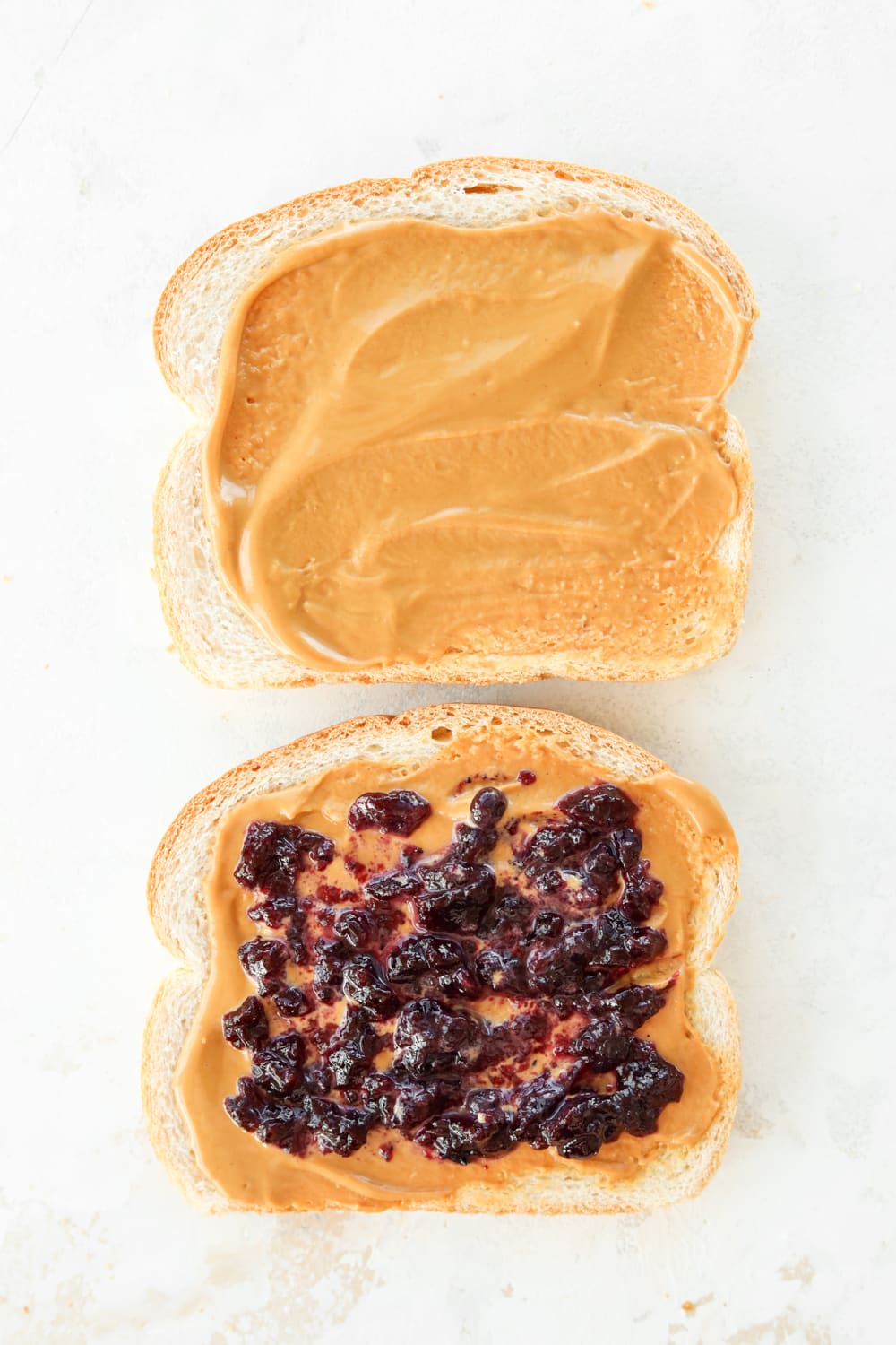 A slice of bread with peanut butter on it and another slice of bread with peanut butter and jelly on it.