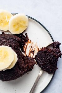 Part of a chocolate protein mug cake and a white plate with a spoon on it that has a piece of the mug cake on the spoon.