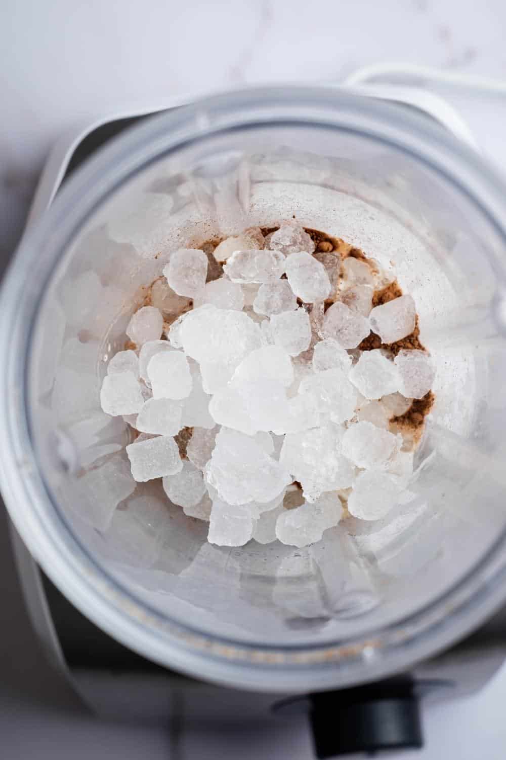 A bunch of ice cubes on top of protein powder in a blender.