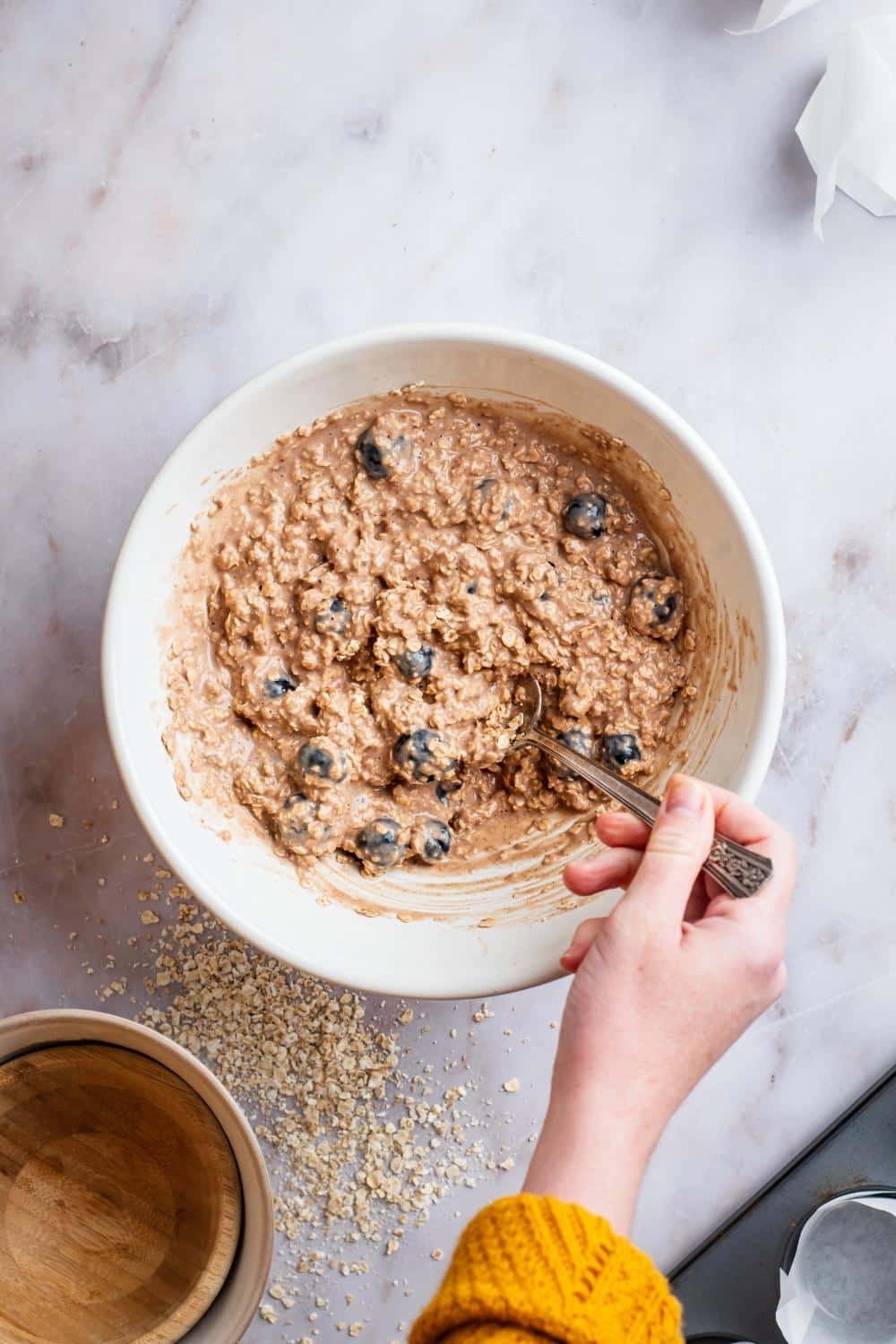 A hand mixing together blueberry protein muffin ingredients.