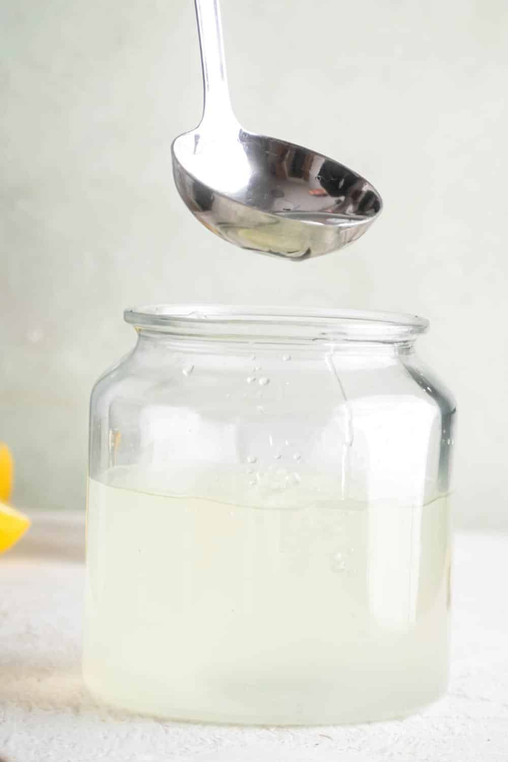 A ladle with lemonade in it hovering over a large bowl that is filled with lemonade.