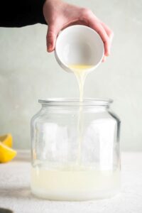 A hand pouring lemon juice into a large glass bowl.