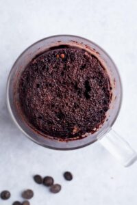 A chocolate protein mug cake in a glass mug on top of a white counter.