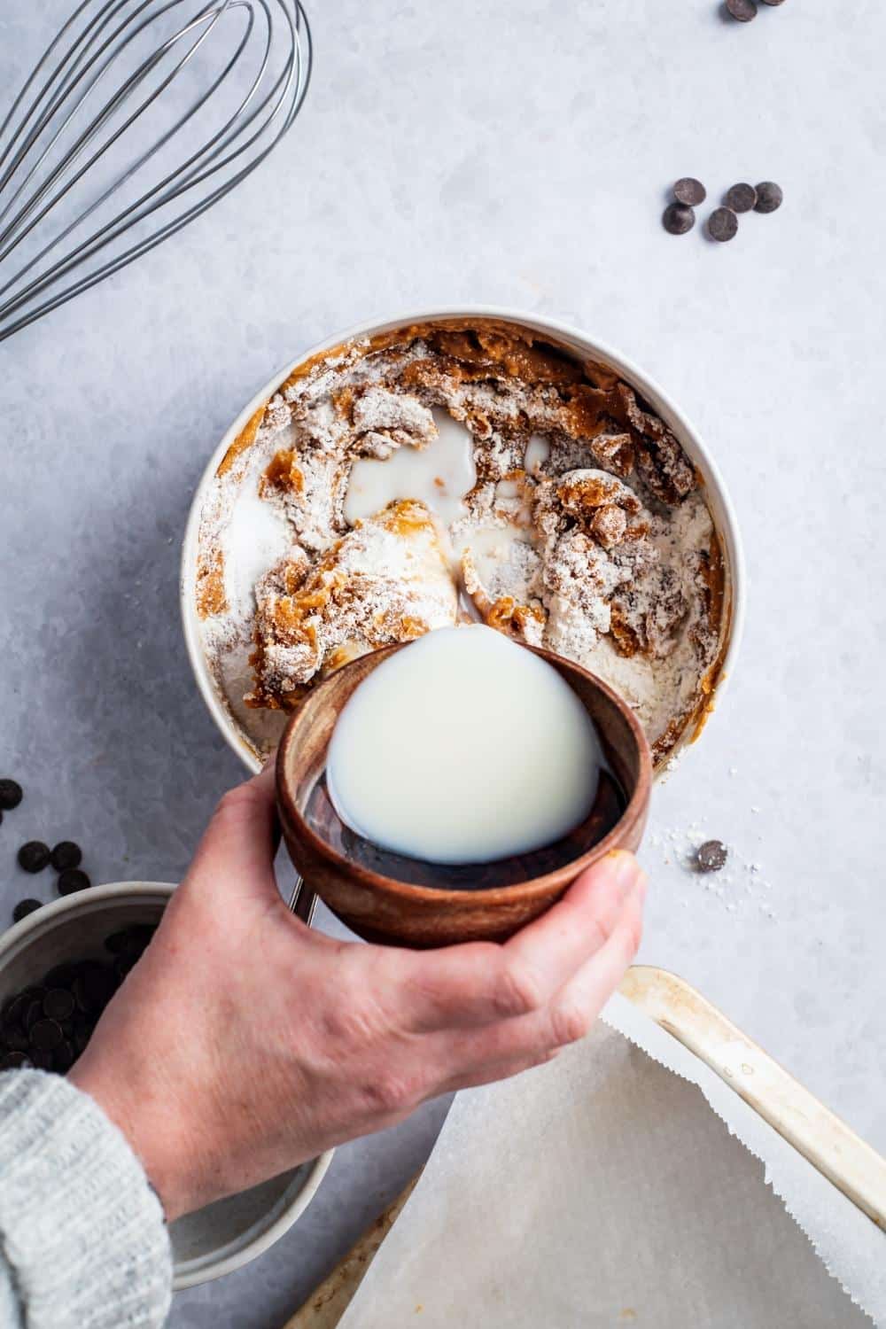 A hand pouring milk into a bowl of protein cookie ingredients.