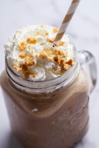 Crushed peanuts on top of whipped cream on top of a keto smoothie in a glass mug.