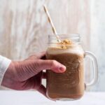 A hand holding a glass mug that is filled with a keto protein shake.